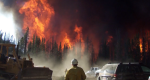 Photo of a firefighter standing next to a dozer and truck looking toward the fire.