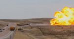 Photo of a gas fire plume in a field with fire trucks on the road.