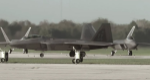 A fighter jet on tarmac with two other fighter jets lined up in background.